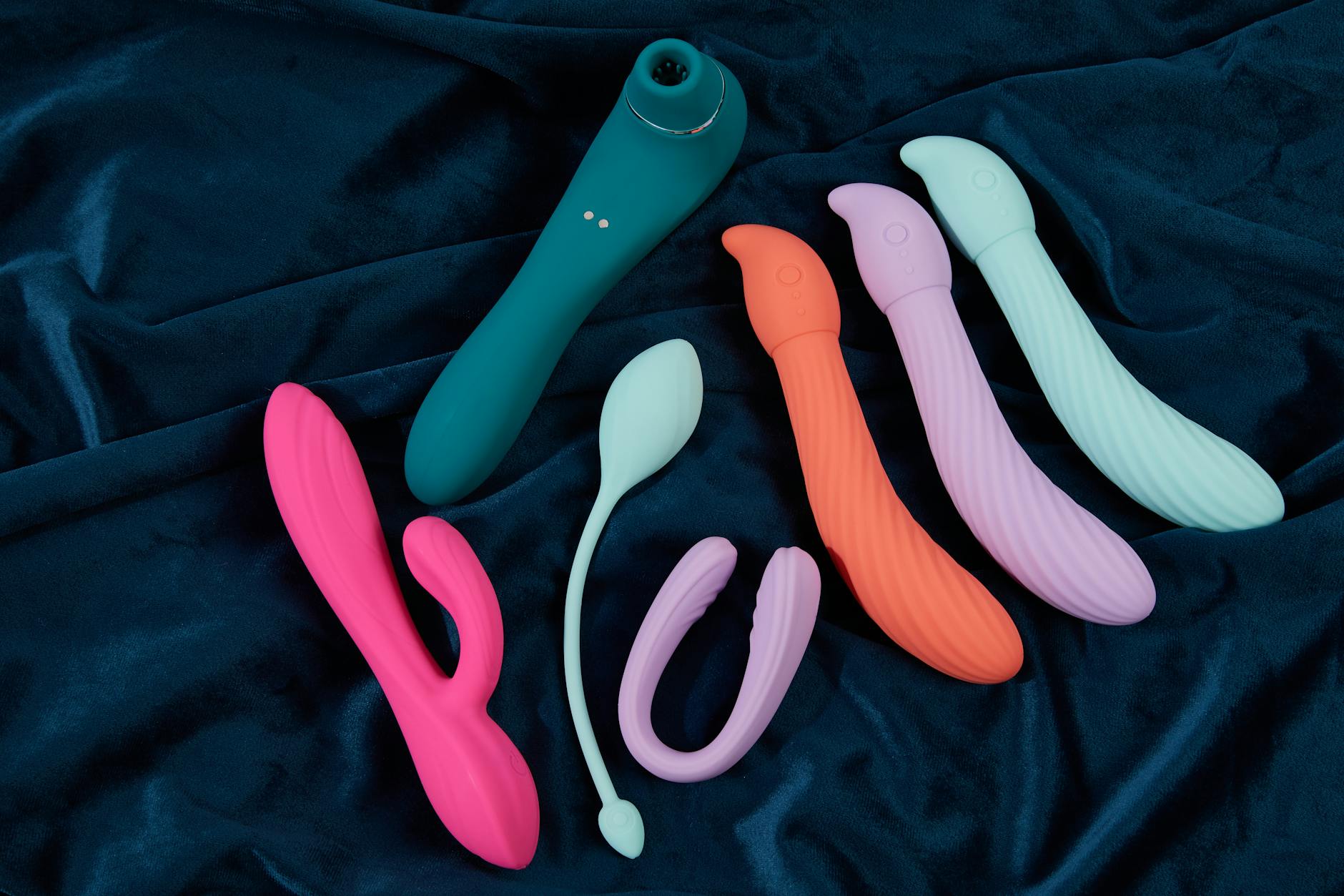Woman holding blue and pink silicone vibrators in a thoughtful pose
