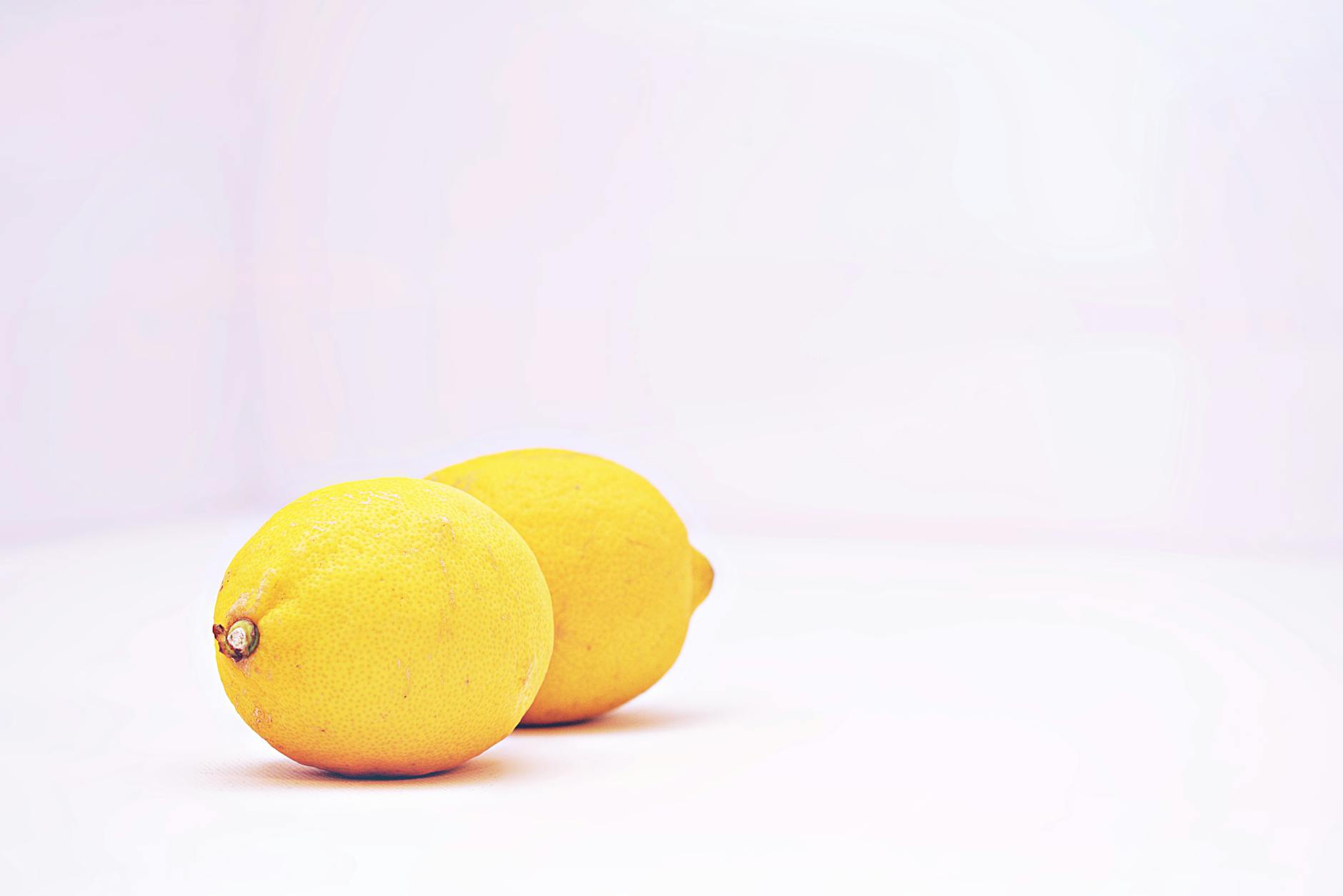 A hand holding a fresh lemon against a soft pink background, surrounded by additional lemons, symbolizing the natural and gentle approach to pleasure.