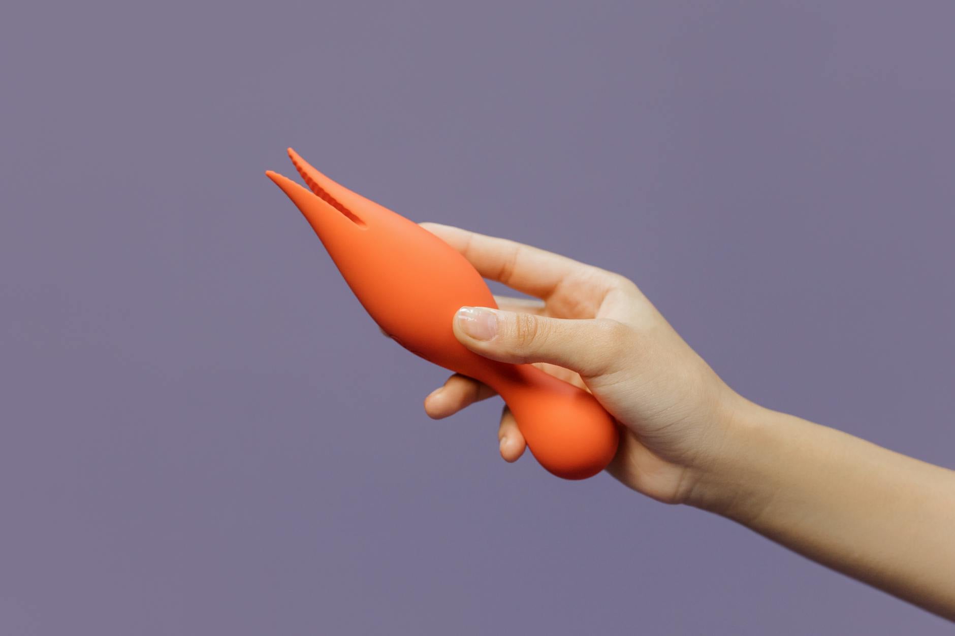 A close-up of a hand holding a lemon-colored vibrator against a minimalistic purple backdrop, showcasing modern sensuality.