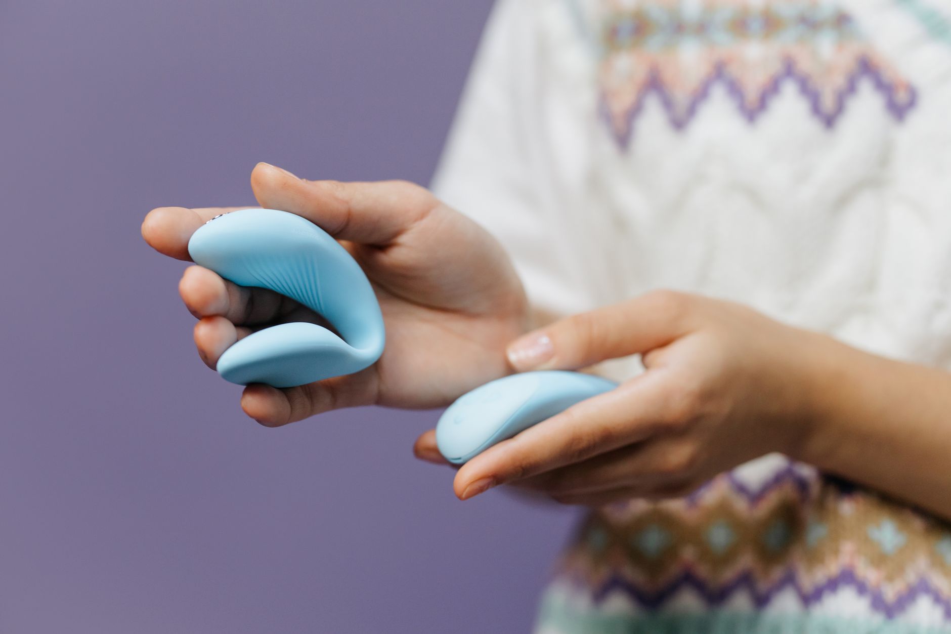 Hands holding a sleek lemon vibrator against a purple background, representing pleasure and calm.